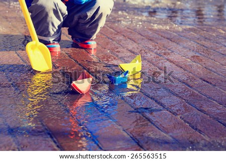 child playing with paper boats in spring water puddle