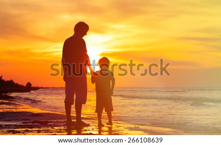 silhouettes of father and son holding hands at sunset sea