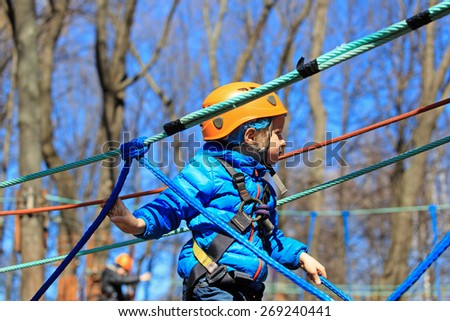 little boy climbing in adventure activity park with helmet and safety equipment