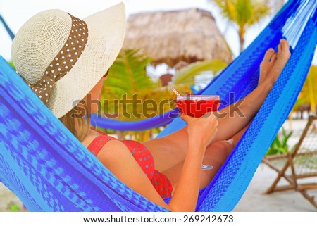 woman with cocktail relaxed in hammock on tropical beach