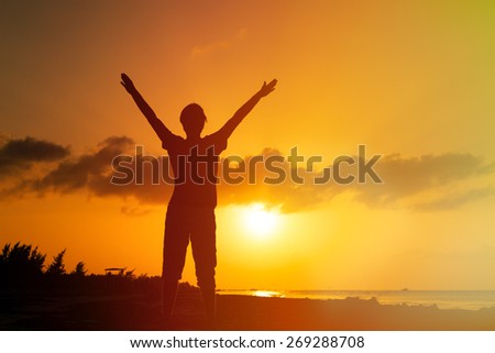 silhouette of man with his hands up on sunset beach