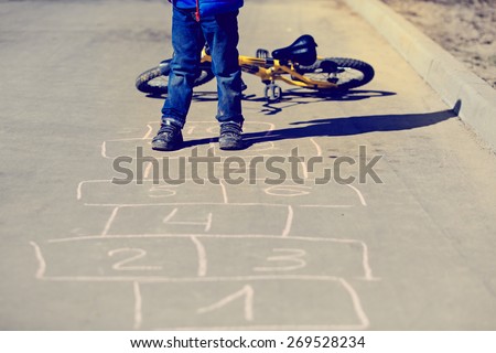 little boy playing hopscotch with bike outside