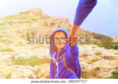 Helping hand- little boy helped by parent on hiking in mountains