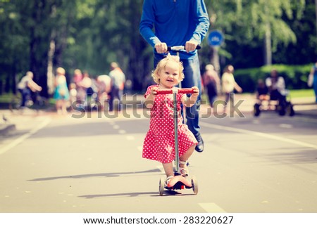 happy little girl and father on scooters in the city, family sport