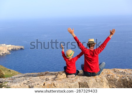 father and son sitting on top of a mountain expressing joy with their arms stretched up towards sky