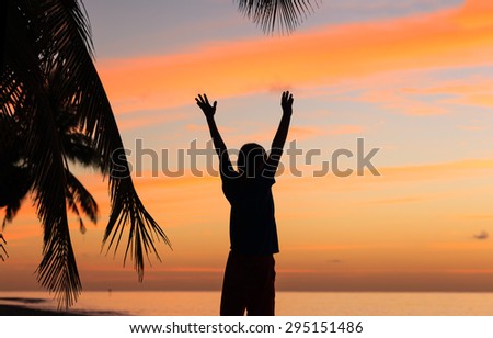 silhouette of  happy man with his hands up on sunset beach