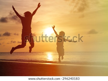father and son jumping at sunset beach, happy family