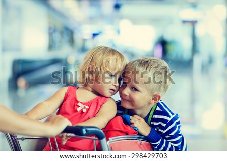 Happy cute little girl and boy at airport riding on luggage cart
