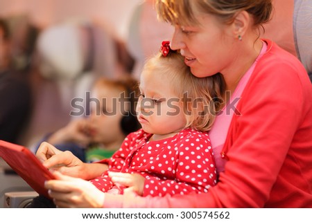 mother and little daughter looking at touch pad in plane, family travel