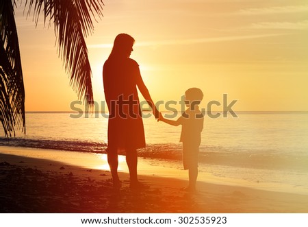 silhouettes of mother and son holding hands at sunset sea