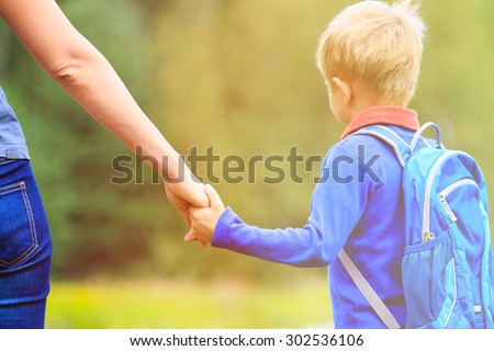 Mother holding hand of little son with backpack outdoors, back to school