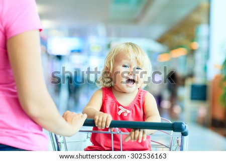 mother and cute little daughter on luggage cart in the airport, family travel