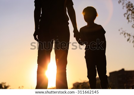 silhouette of father and son holding hands at sunset sky