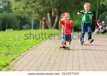 little boy and toddler girl riding scooters in summer park, kids sport