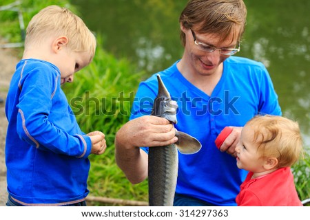 father and two kids holding fish they caught on the lake