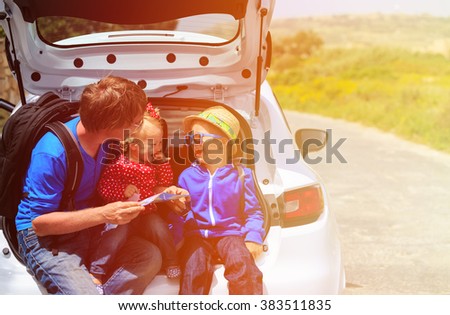 father with two kids looking at map while travel by car