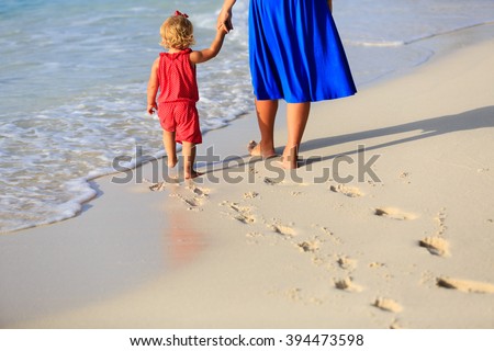 mother and daughter walking on beach leaving footprint in  sand