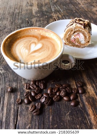 Cup of latte or cappuccino with coffee beans and cake roll on wooden desk