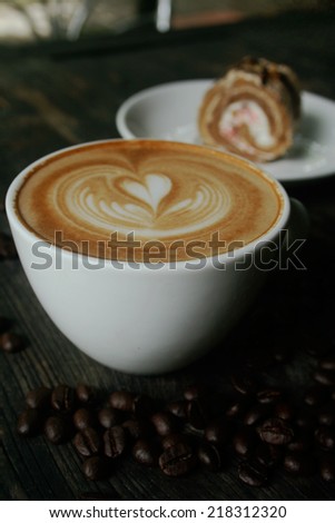 Cup of latte and cappuccino and coffee beans with cake roll on wooden desk