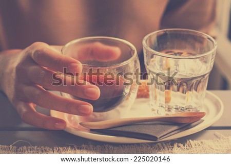 hand holding a freshly brewed cup of hot black coffee americano,drinking water in retro filter effect or instagram filter