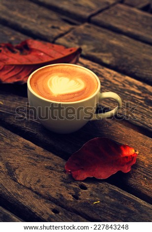 Fall or Autumn morning Cup of latte or cappuccino coffee setting on wooden table with fall leaves  with pastel mood vintage retro filter effect