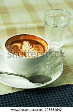 Cup of latte or cappuccino coffee and glass of water on table cloth