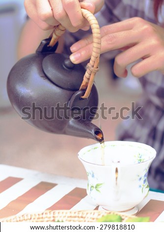 women's hand pouring tea from teapot in retro filer effect lighting or instagram filter