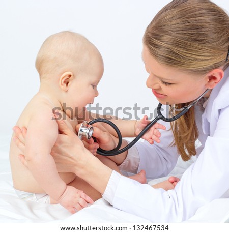 Cute smiling baby girl playing with stethoscope of woman doctor therapist, pediatrician, physician. Happy child sitting at the young female doctor.