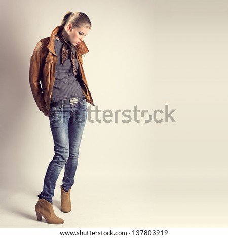 Fashion girl. Beautiful glamour stylish model in leather jacket, neckerchief, jeans, high heels. Young Caucasian woman posing in studio.