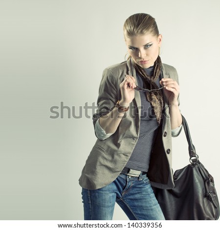 Fashion girl. Attractive blue eyes female holding a leather bag and sunglasses. Beautiful blue eyes Caucasian woman model posing in studio.
