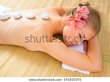 Spa massage. Beautiful young Caucasian blond female with flower in her hair in wellness center.