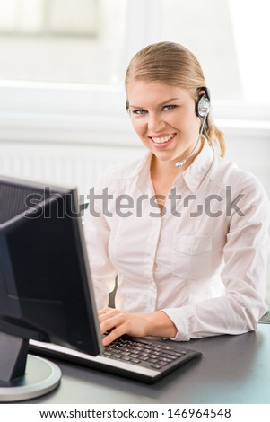 Young professional female phone assistant of call center. Beautiful blond Caucasian woman hotline consultant sitting at the desk in the office.
