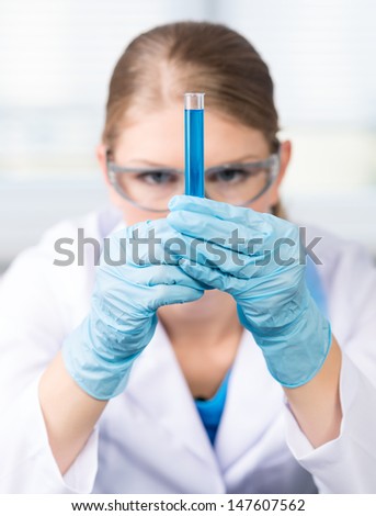 Portrait of researcher woman working with laboratory glass tube filled with chemical solution. Young female technician in medical gloves and protective glasses.