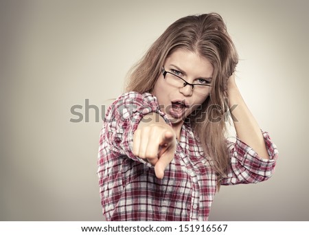 Beautiful screaming woman in eyeglasses pointing forefinger at you. Young attractive Caucasian female model stretching her hand forward, looking at camera, posing at studio.
