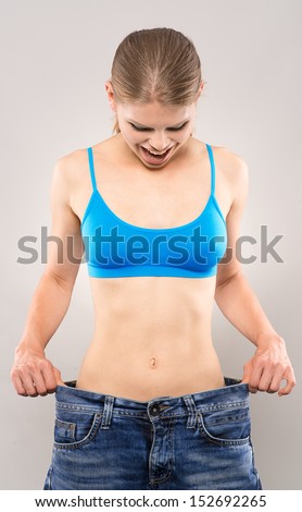 Joyful fitness girl wearing big jeans, looking at her slim waist. Healthy lifestyle concept.