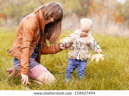 Happy family playing with leaves on green meadow. Young beautiful woman and her toddler girl having fun outdoors.