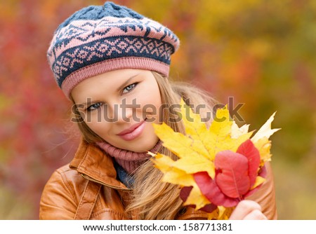 Beautiful female with autumn leaves walking in colorful forest. Nice smiling girl relaxing in autumn park.