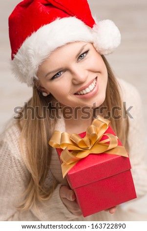 Portrait of happy smiling Santa lady wearing warm knitted clothes with Christmas gift.Young attractive Caucasian female model celebrating holidays at home in freezing winter days.