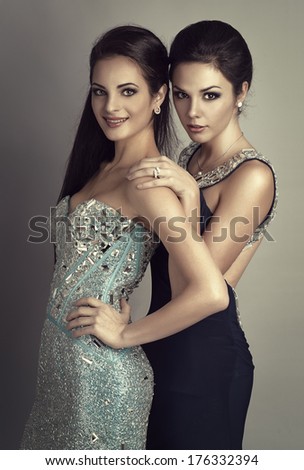 Fashion ladies wearing expensive brilliant clothes and jewelery. Young and rich people posing in studio.