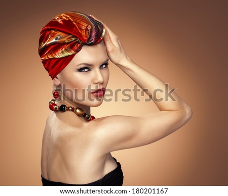 African style. Pretty glamour Caucasian model with red turban and expensive golden jewelery posing in studio.