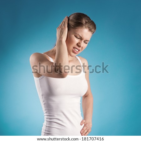 Young female suffering from ear pain over blue background. Medical and health concept.