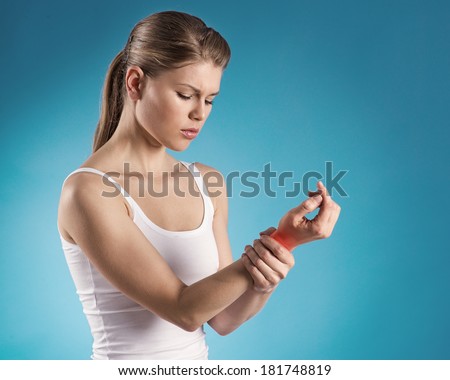 Young woman holding her painful wrist over blue background. Sprain pain location indicated by red spot.
