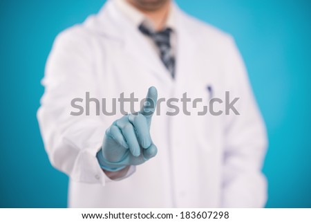 Male surgeon in surgical gloves pointing something over blue background.