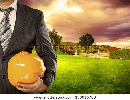 Construction project in countryside. Male engineer wearing business suit standing over green field background.