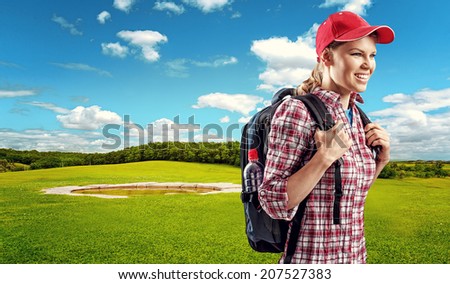 Happy female traveler hiking on green field. Young woman trekker with backpack walking through golf park.