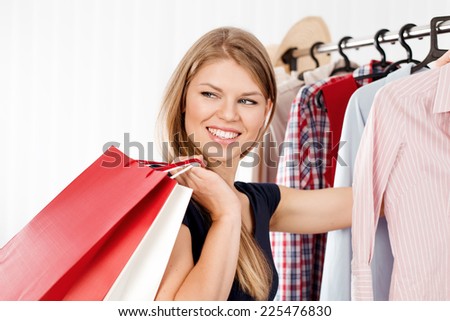 Young joyful woman with colorful shopping bags indoors in retail store. Spree female shopper choosing dress in clothing shop.