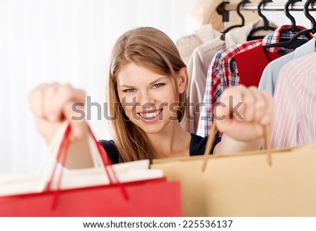 Lovely woman customer with shopping bags standing at clothing rack in retail store. Young pretty female clothes shop owner giving purchase to customer.