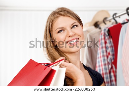 Close up portrait of young pretty woman buyer with purchases in shopping mall. Happy female customer standing with shopping bags at clothes rack.