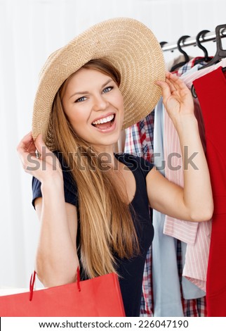 Shopping woman dreaming of travel and vacation. Young attractive Caucasian model with gift bags in retail clothes shop choosing hat.