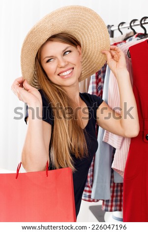 Shopping woman dreaming of travel and vacation. Young attractive Caucasian model with gift bags in retail clothes shop choosing hat.